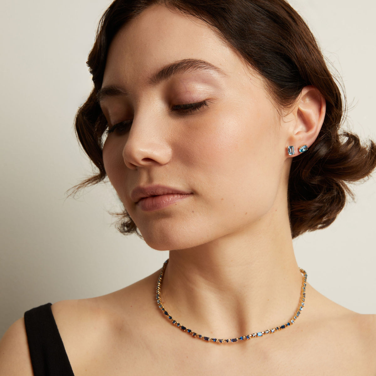 Close-up of a woman wearing a blue necklace and earrings against a neutral background. Model
