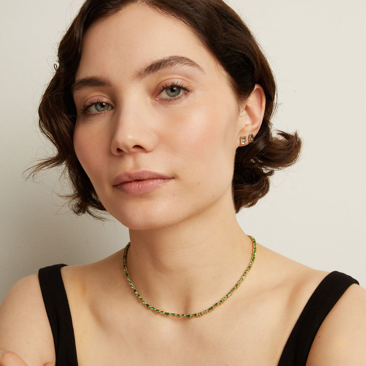 Woman wearing a green tennis necklace and earrings on a neutral background. Model