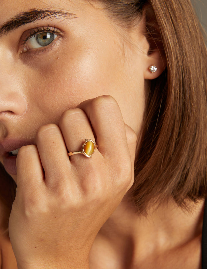 Close up of woman wearing a gold ring with a bold yellow gemstone on neutral background.