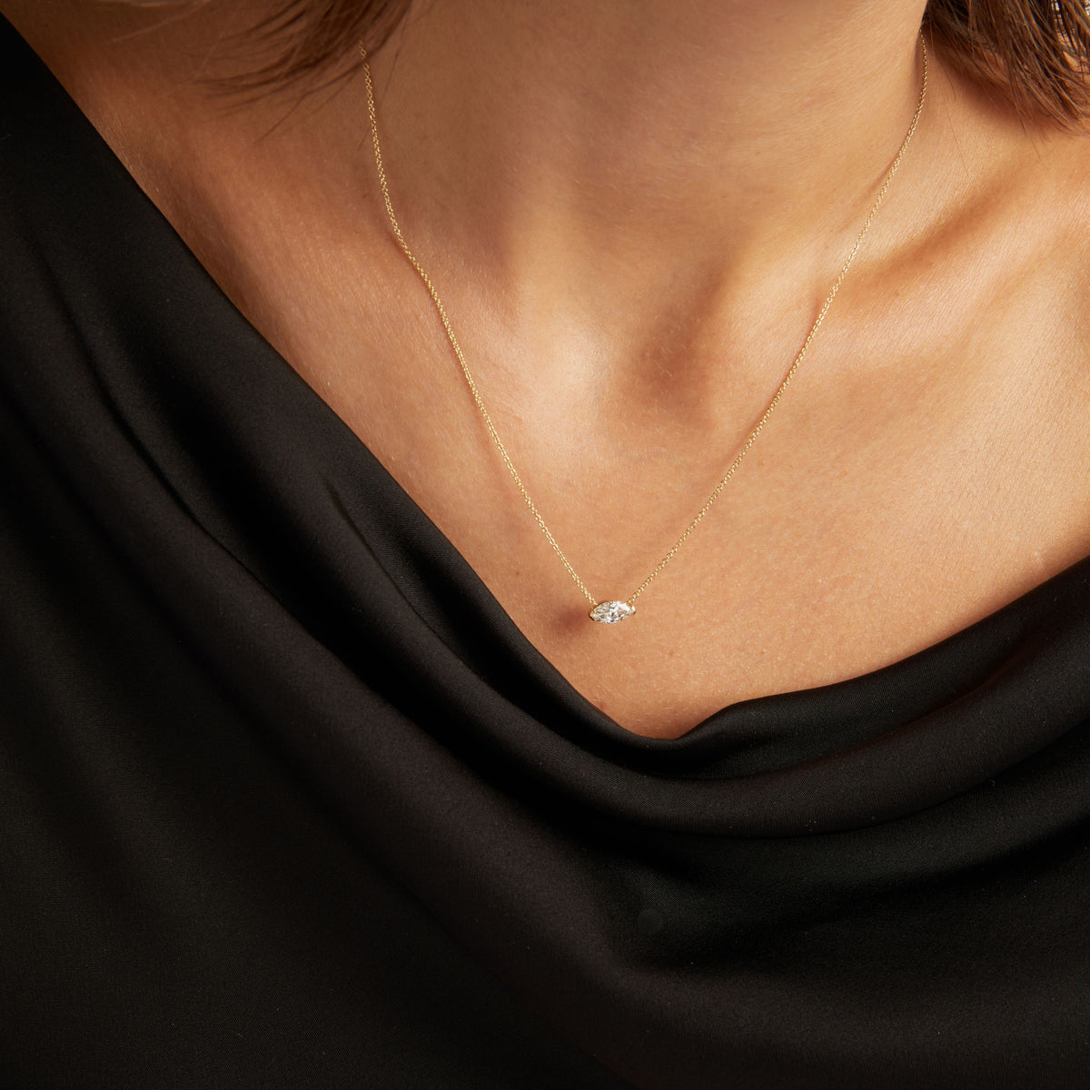 Model. Close up of woman wearing a black top with a marquise diamond solitaire necklaces on a beige background.