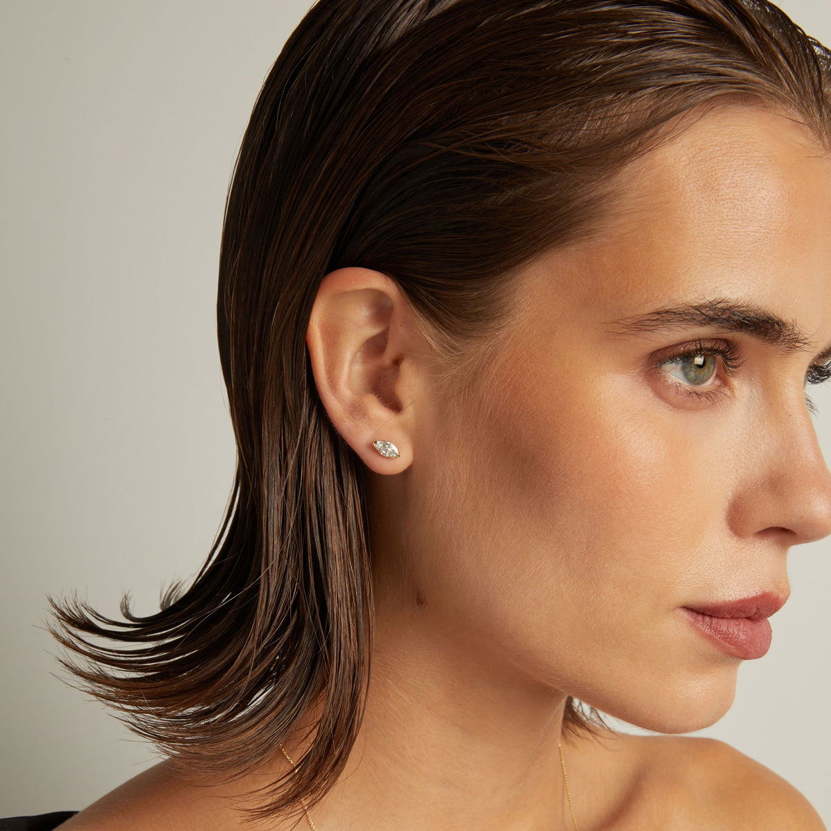Close up of woman wearing a marquise shaped diamond stud earring on a beige background.