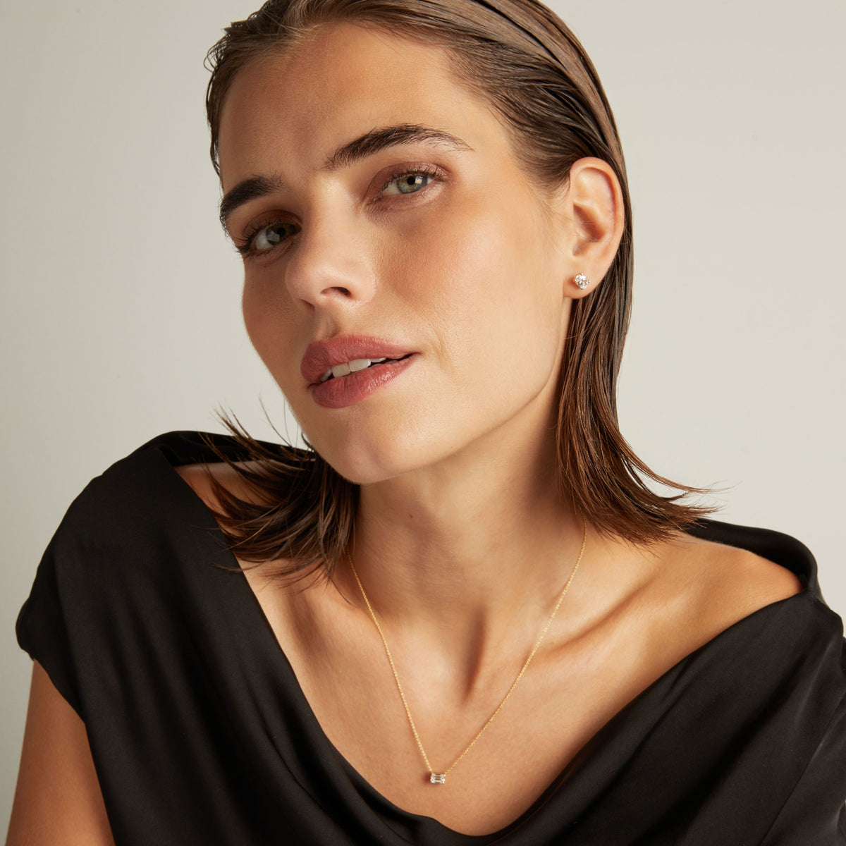 Model. Close up of woman wearing an oval diamond stud earring on a beige background.