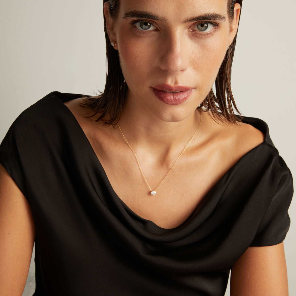 Model. Close up of woman wearing a black top with an oval shaped diamond solitaire necklaces on a beige background.