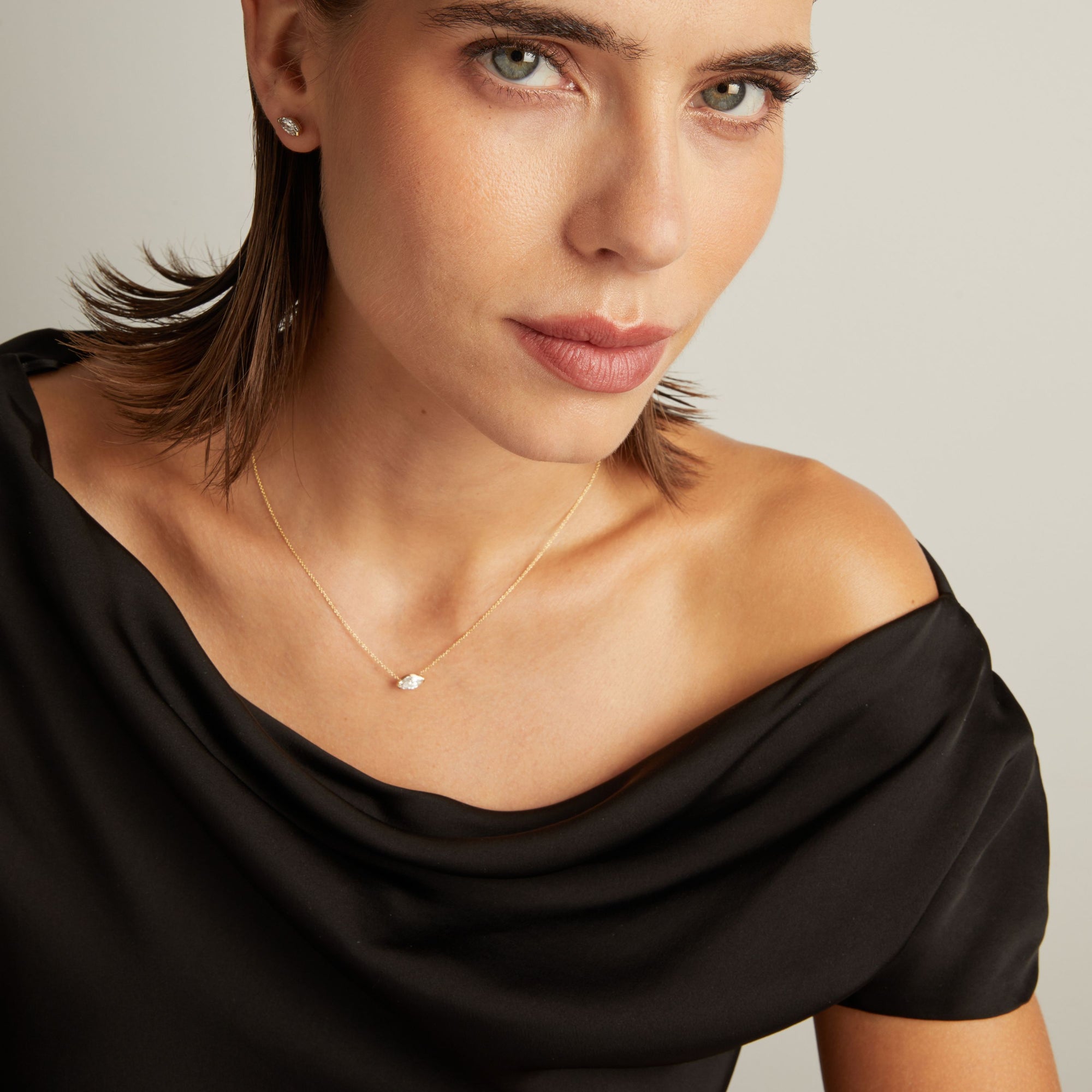 Close up of woman wearing a black top with a marquise shaped diamond solitaire necklaces on a beige background.