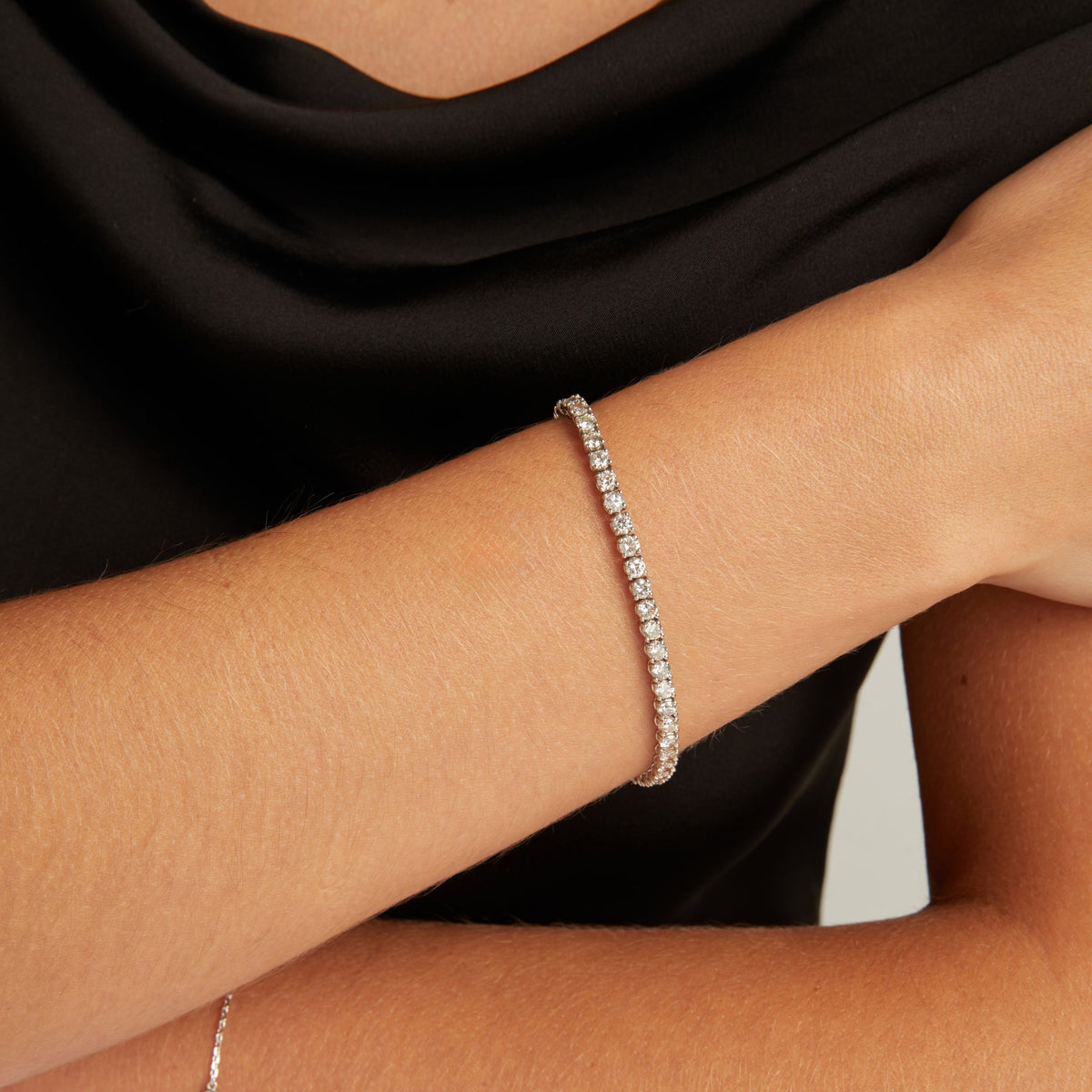 Model. Close up of a woman wearing a black top with a diamond tennis bracelet on beige background.