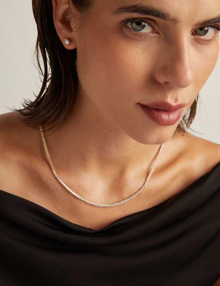 Model. Close up of a woman in a black top wearing a diamond tennis necklace on beige background.