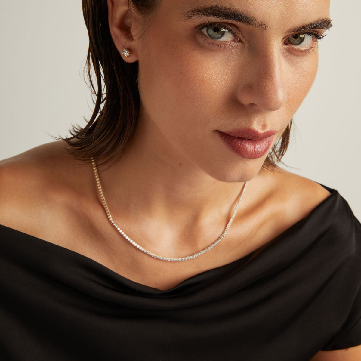 Model. Close up of a woman in a black top wearing a diamond tennis necklace on beige background.
