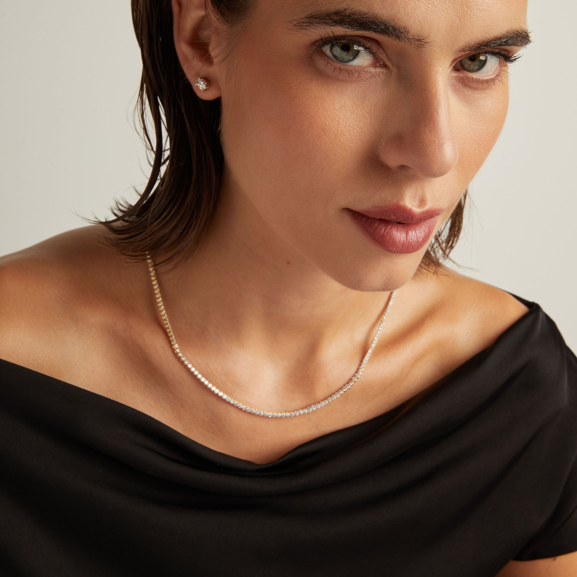Model. Close up of a woman in a black top wearing a diamond tennis necklace on beige background.