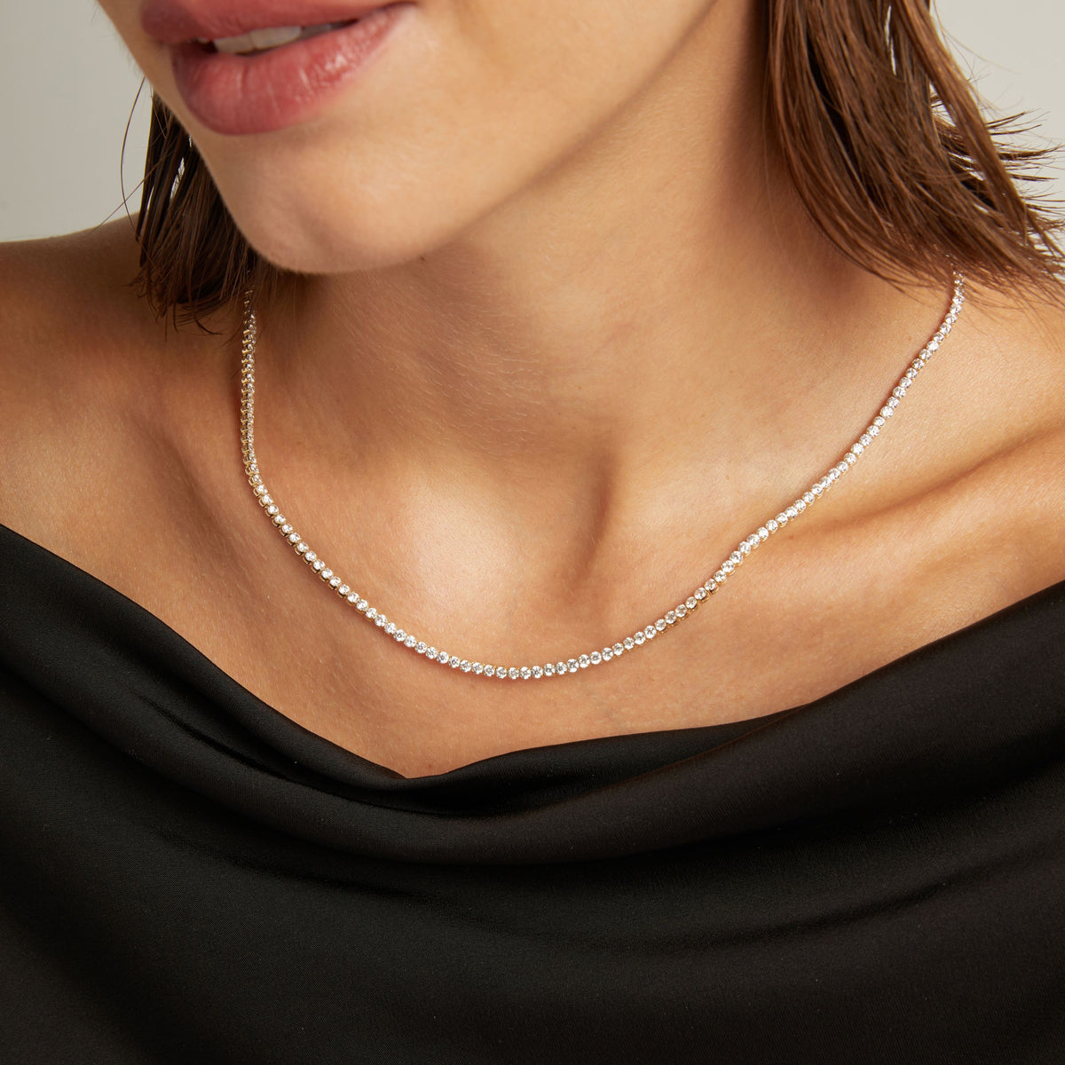 Model. Close up of a woman in a black top wearing a diamond tennis necklace on beige background.