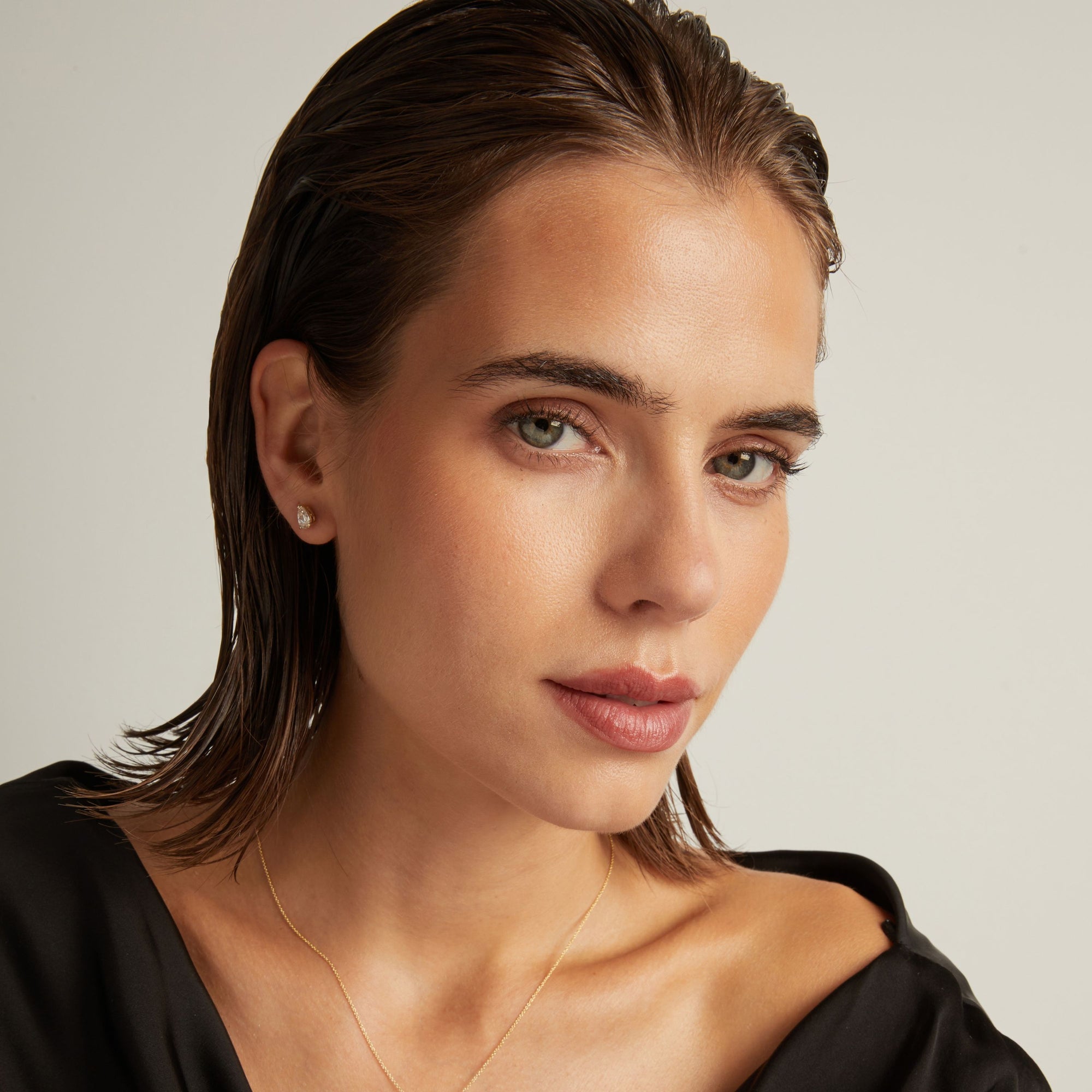 Model. Close up of woman wearing a pear diamond stud earring on a beige background.