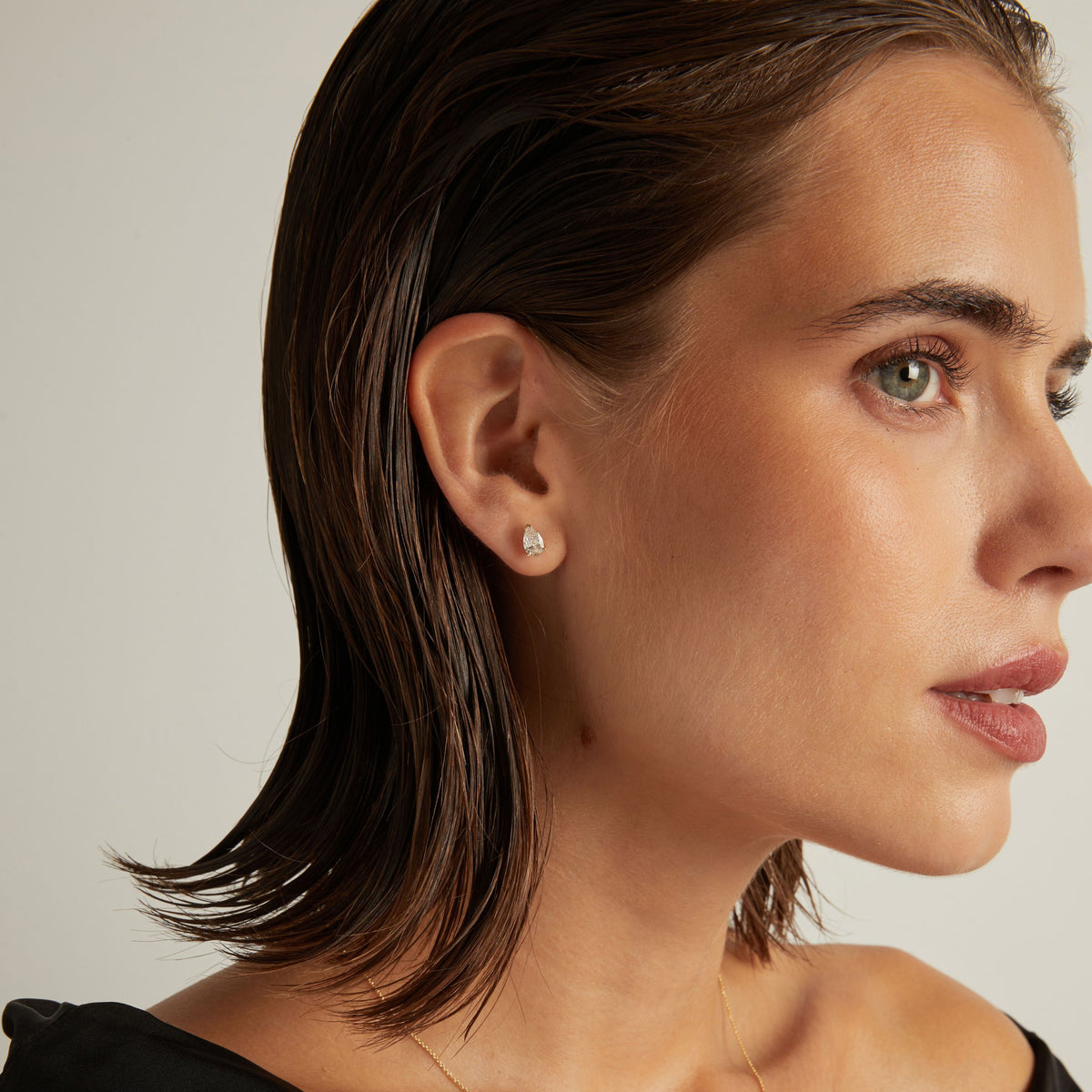 Model. Close up of woman wearing a pear diamond stud earring on a beige background.