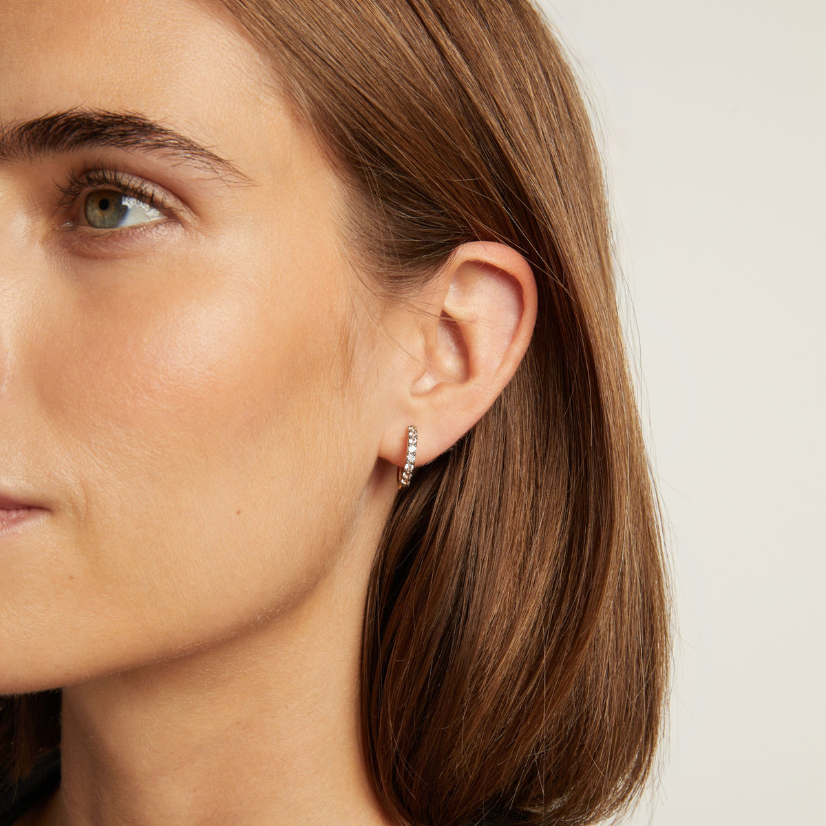 Model. Close up of woman wearing black rhodium huggie earrings on neutral background.