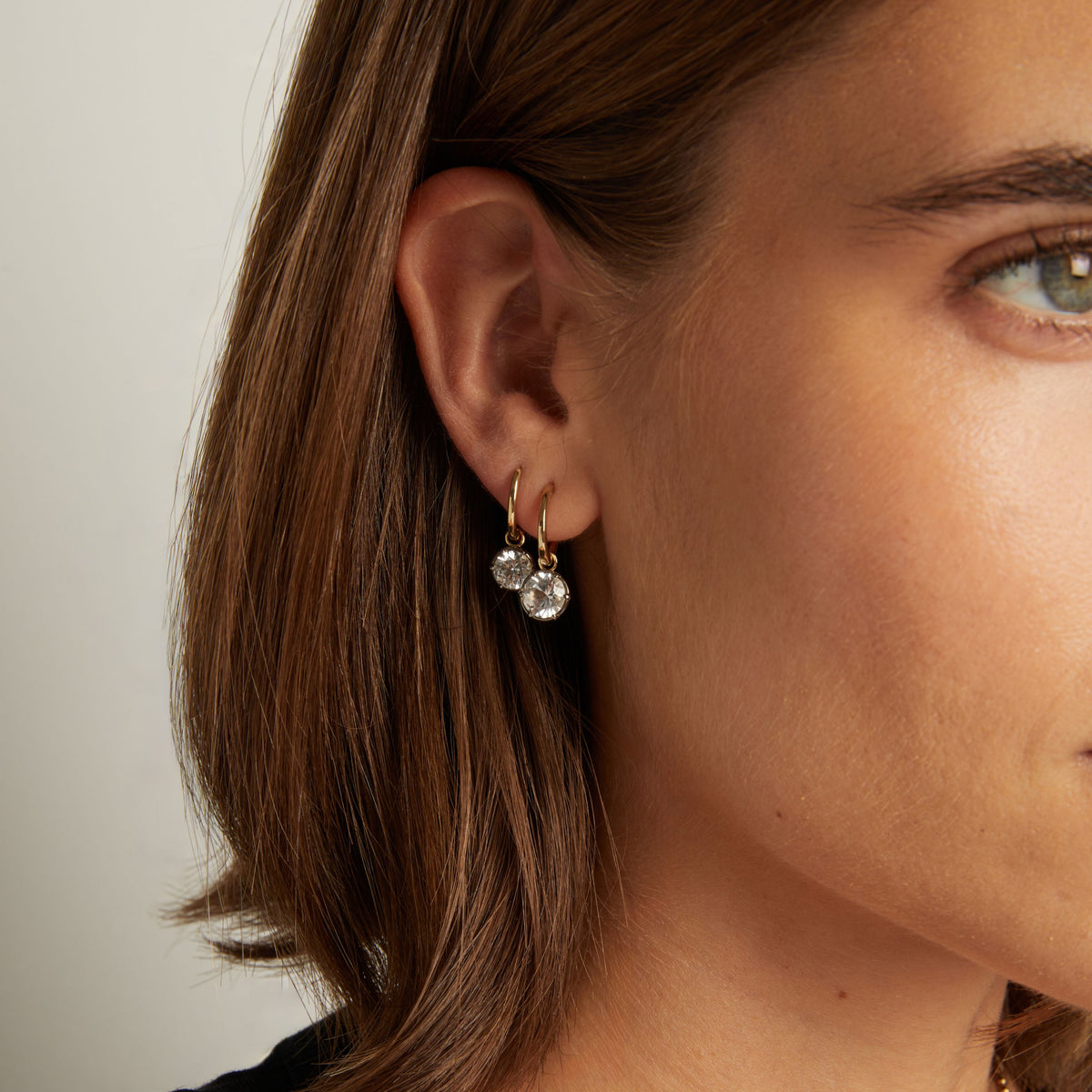 Model. Close up of woman wearing  Georgian Drop Huggie Earrings on neutral background. 