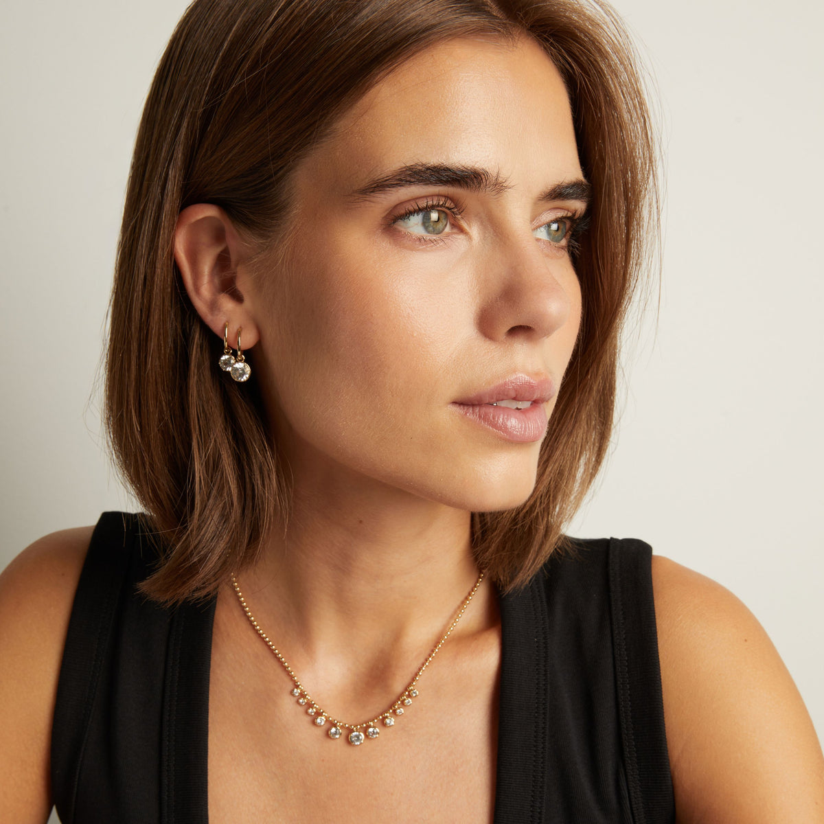 Model. Close up of woman wearing Georgian Drop Huggie Earrings and a matching necklace on neutral background. 