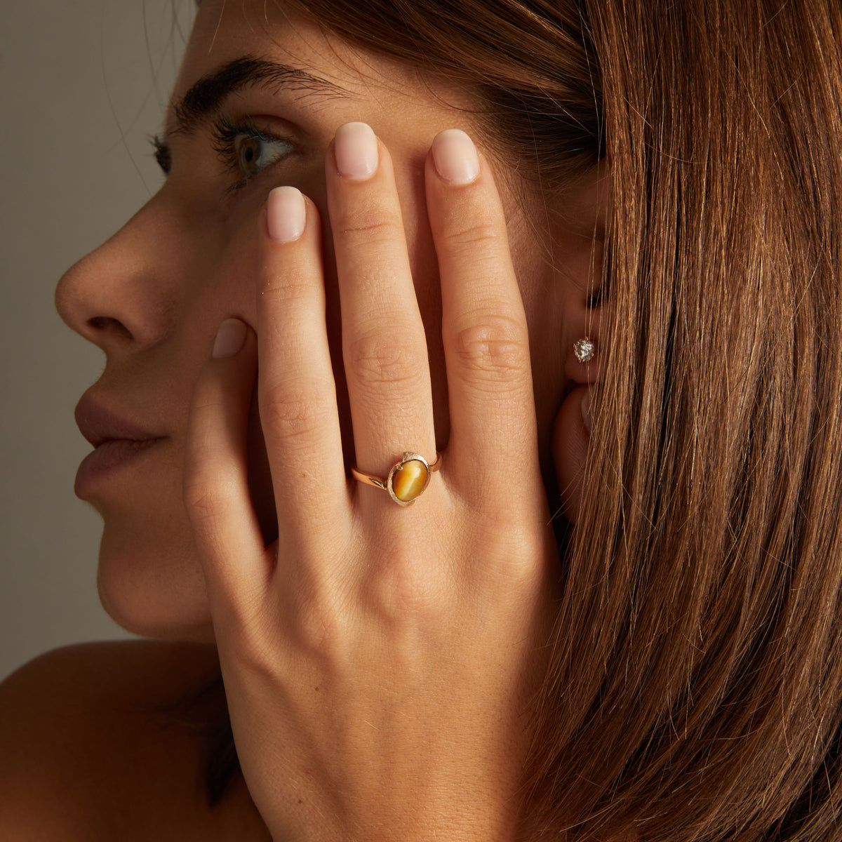 Model. Close up of woman wearing a gold ring with a bold yellow gemstone on neutral background.