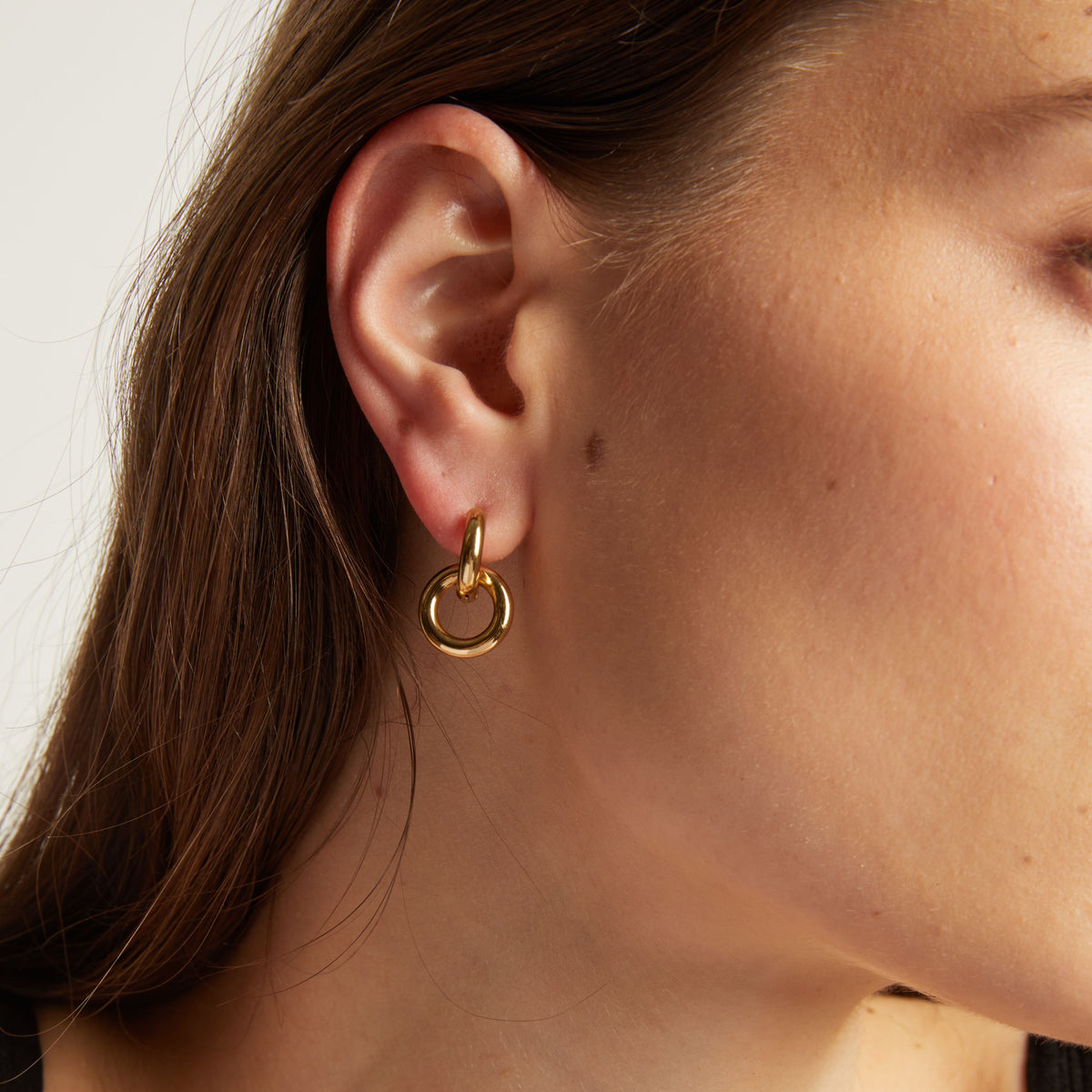 Close up of a person wearing a gold hoop earring with a plain background.
