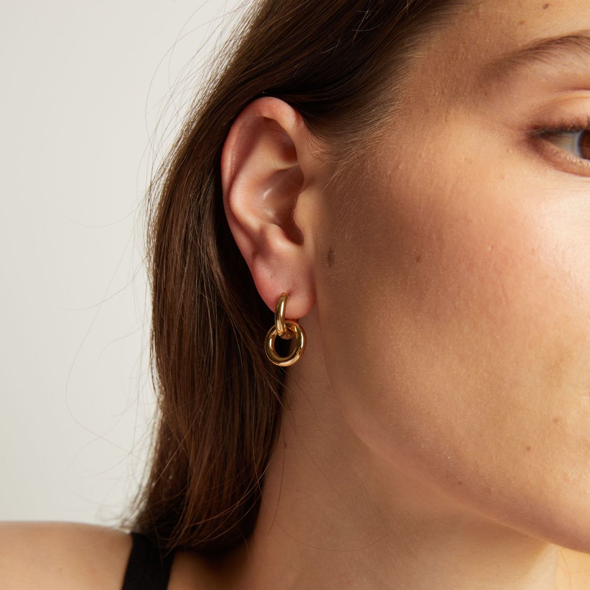 Close up of a person wearing a gold hoop earring with a plain background.