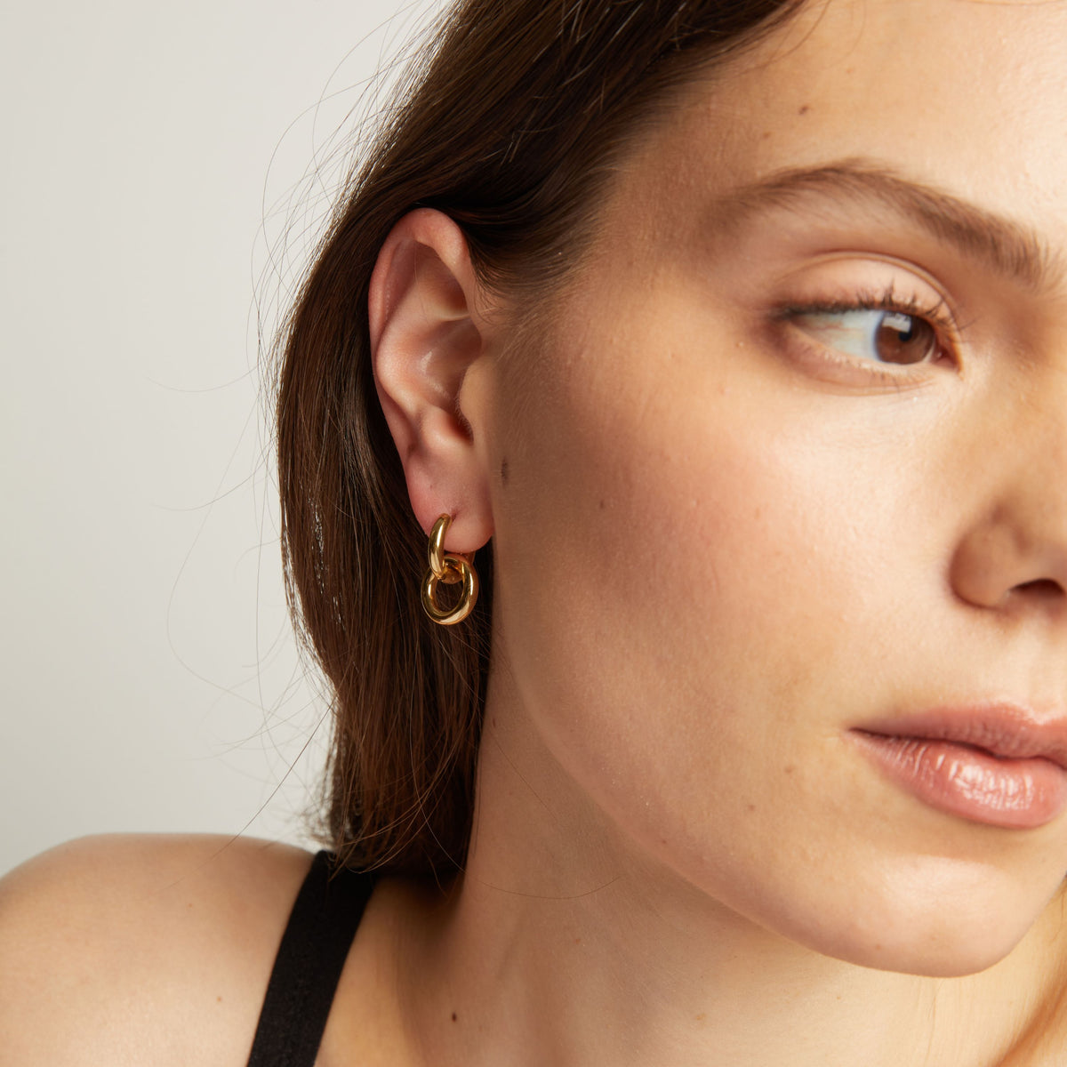 Model. Close up of a person wearing a gold hoop earring with a plain background.