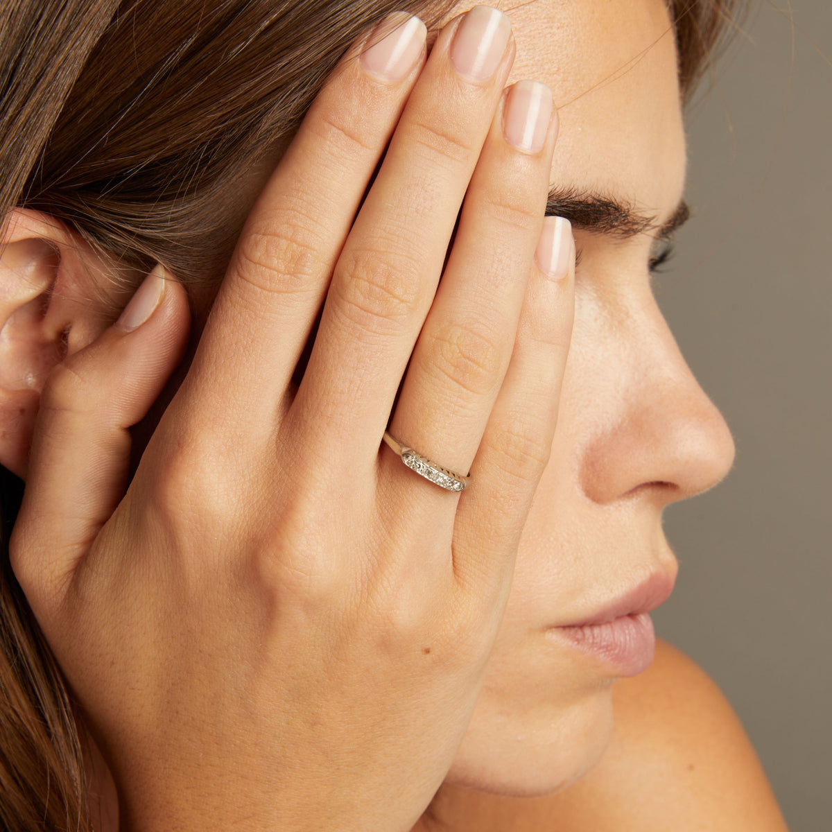 Model. Close up of a woman wearing a ring with a row of diamonds on neutral background.