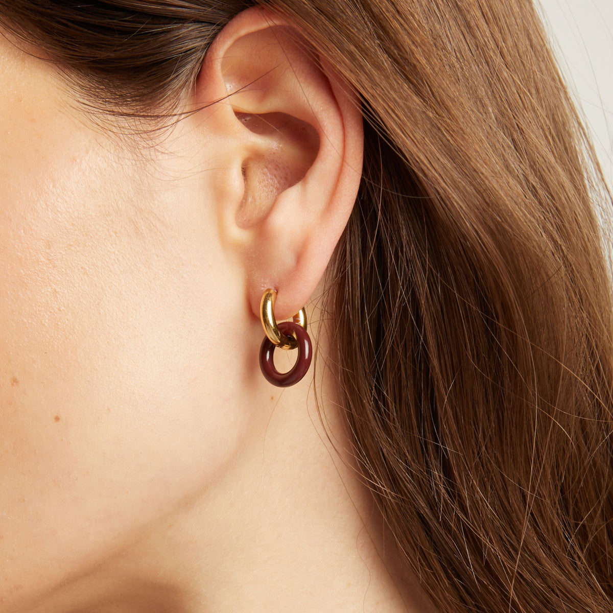  Close up of an ear wearing a gold and maroon hoop earring.