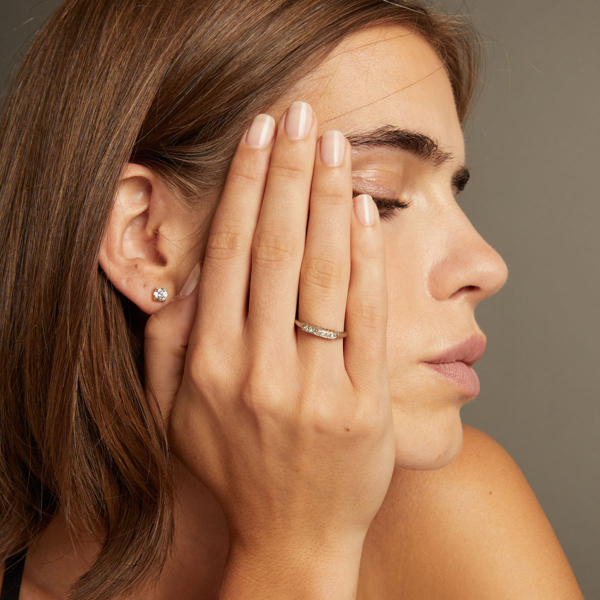Model. Close up of a woman wearing a ring with a row of diamonds on neutral background.