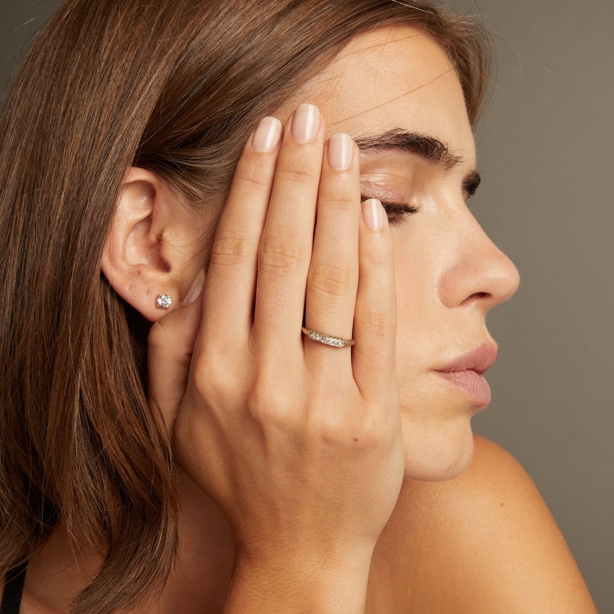 Model. Close up of a woman wearing a ring with a row of diamonds on neutral background.