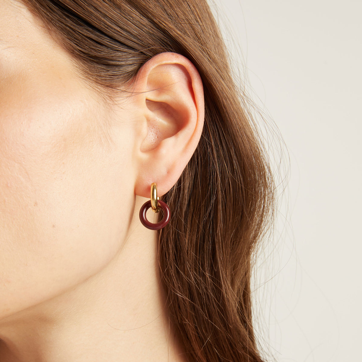 Close up of an ear wearing a gold and maroon hoop earring.