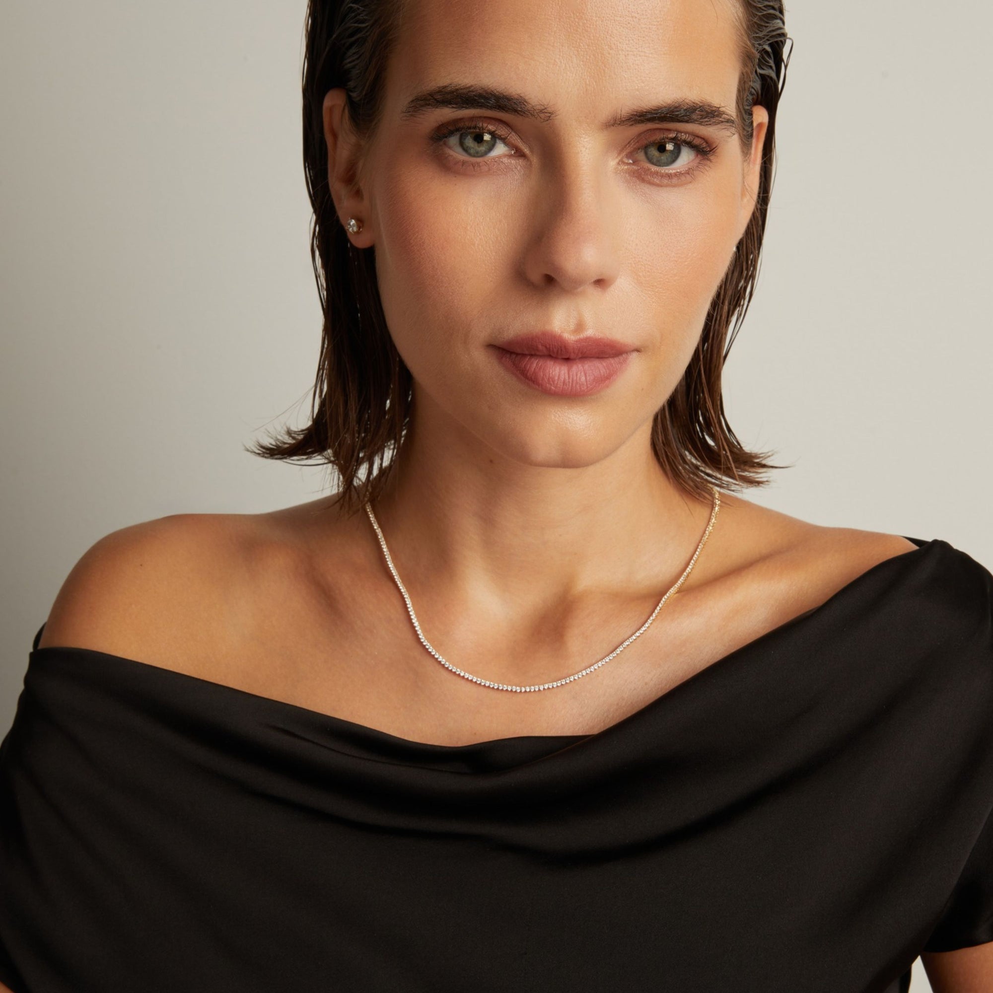 Model. Close up of a woman in a black top wearing a diamond tennis necklace on beige background.