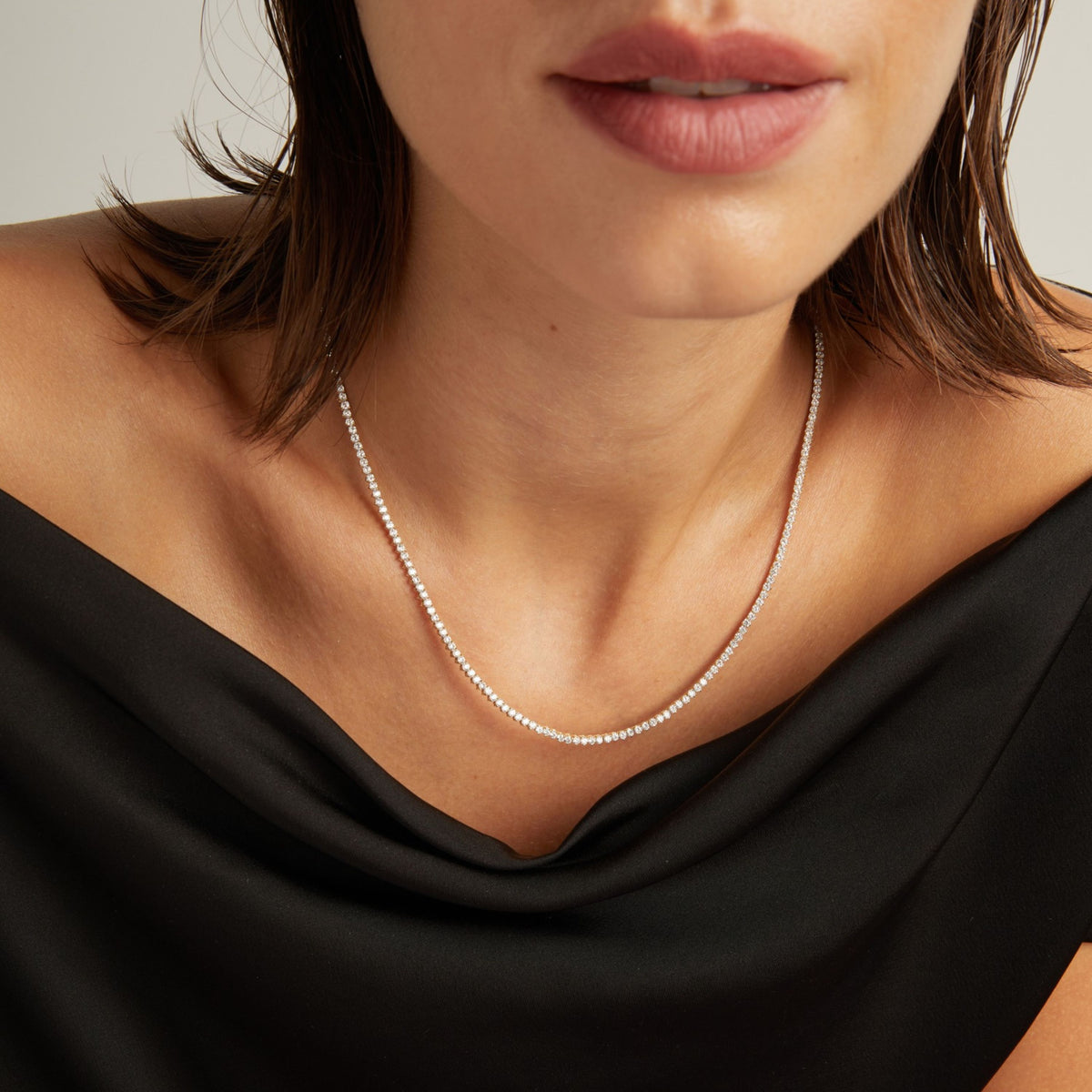 Model. Close up of a woman in a black top wearing a diamond tennis necklace on beige background.