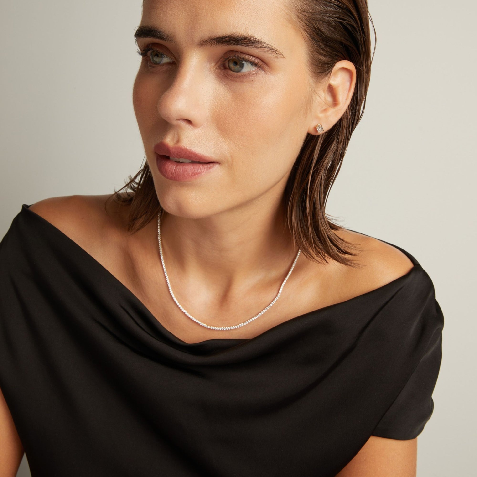 Model. Close up of a woman in a black top wearing a diamond tennis necklace on beige background.