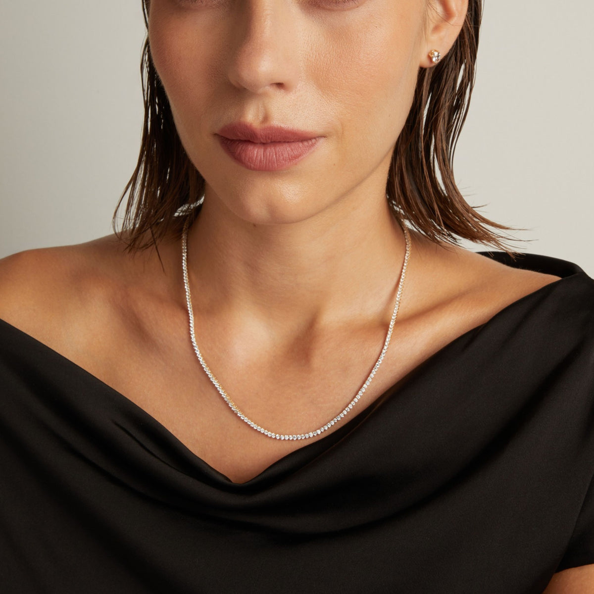 Model. Close up of a woman in a black top wearing a diamond tennis necklace on beige background.