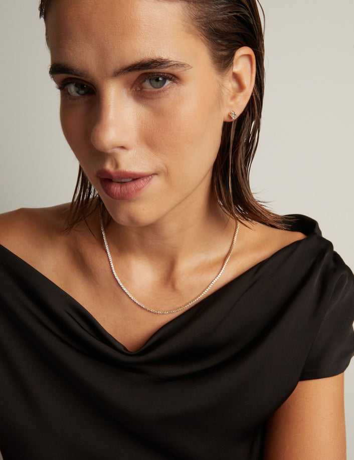 Close up of a woman in a black top wearing a diamond tennis necklace on beige background.
