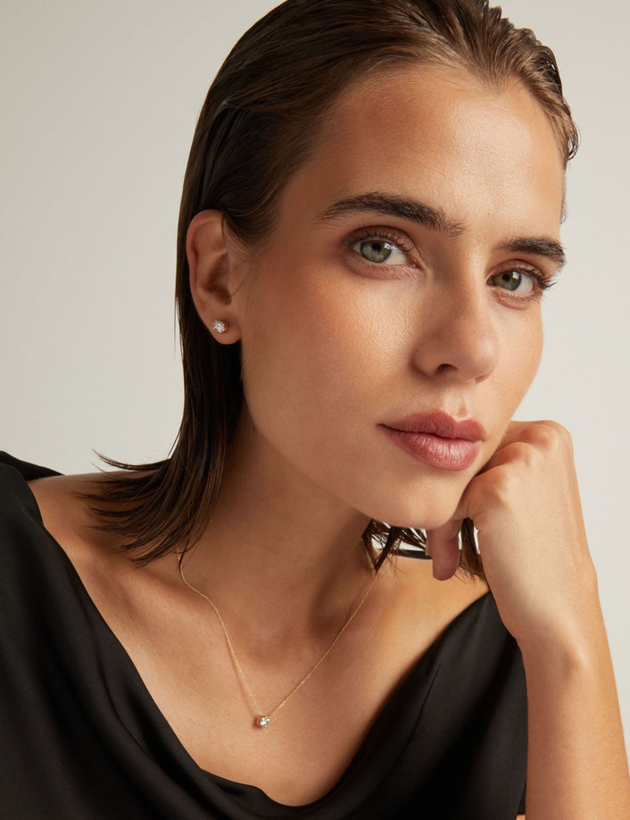 Model. Close up of woman wearing an oval diamond stud earring on a beige background.