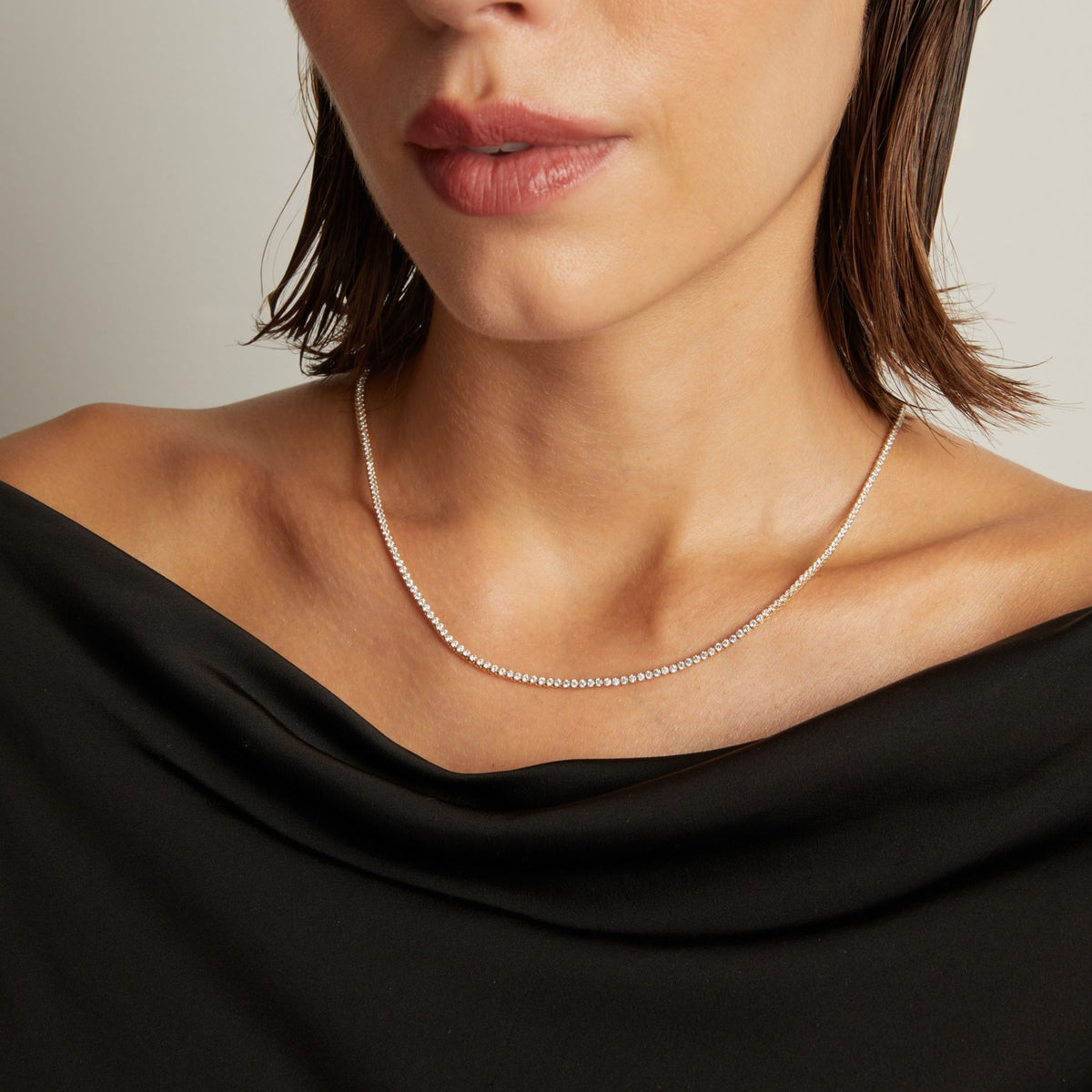 Model. Close up of a woman in a black top wearing a diamond tennis necklace on beige background.