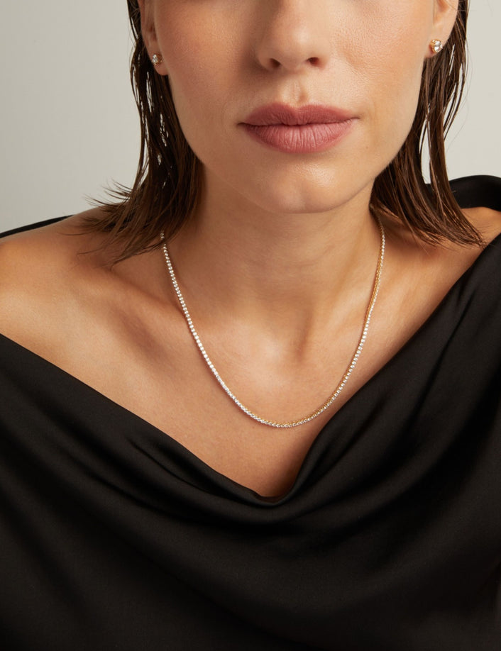 Model. Close up of a woman in a black top wearing a diamond tennis necklace on beige background.