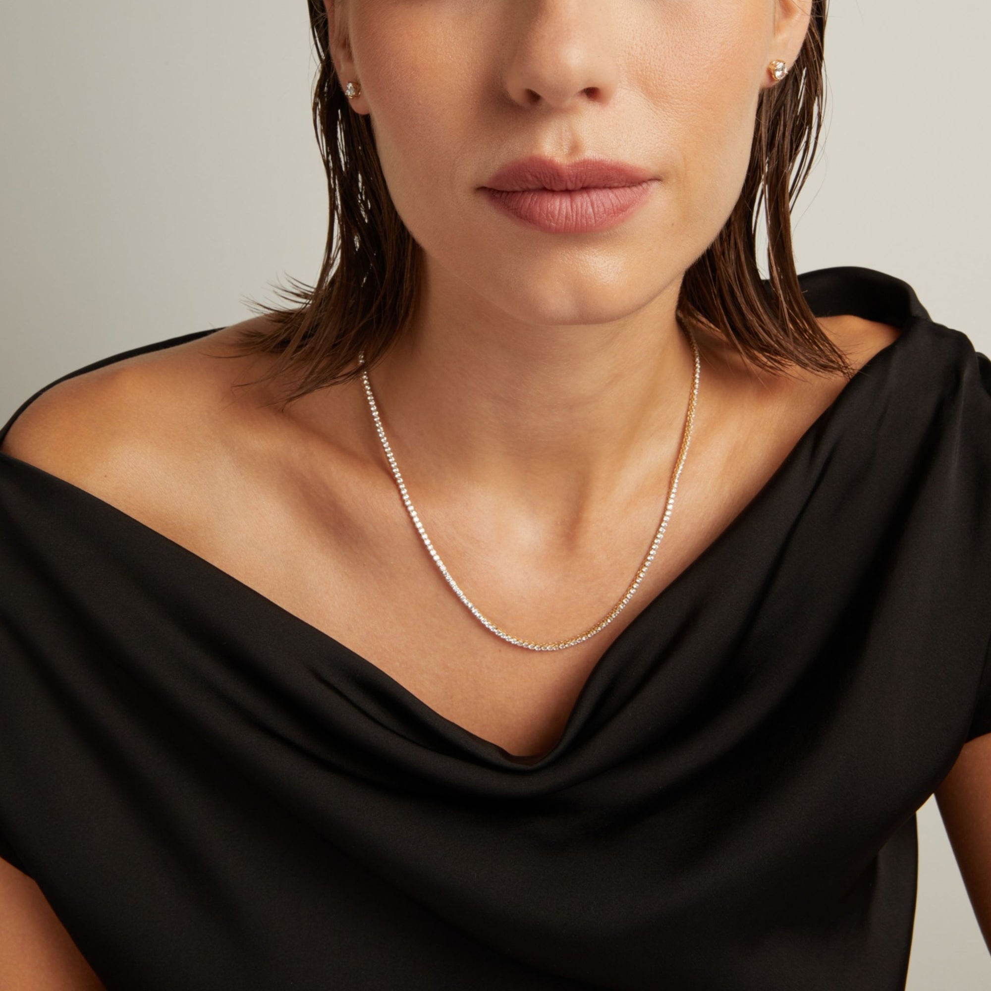 Model. Close up of a woman in a black top wearing a diamond tennis necklace on beige background.