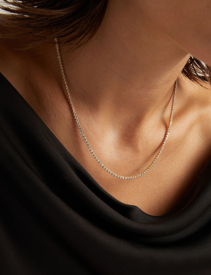 Model. Close up of a woman in a black top wearing a diamond tennis necklace on beige background.