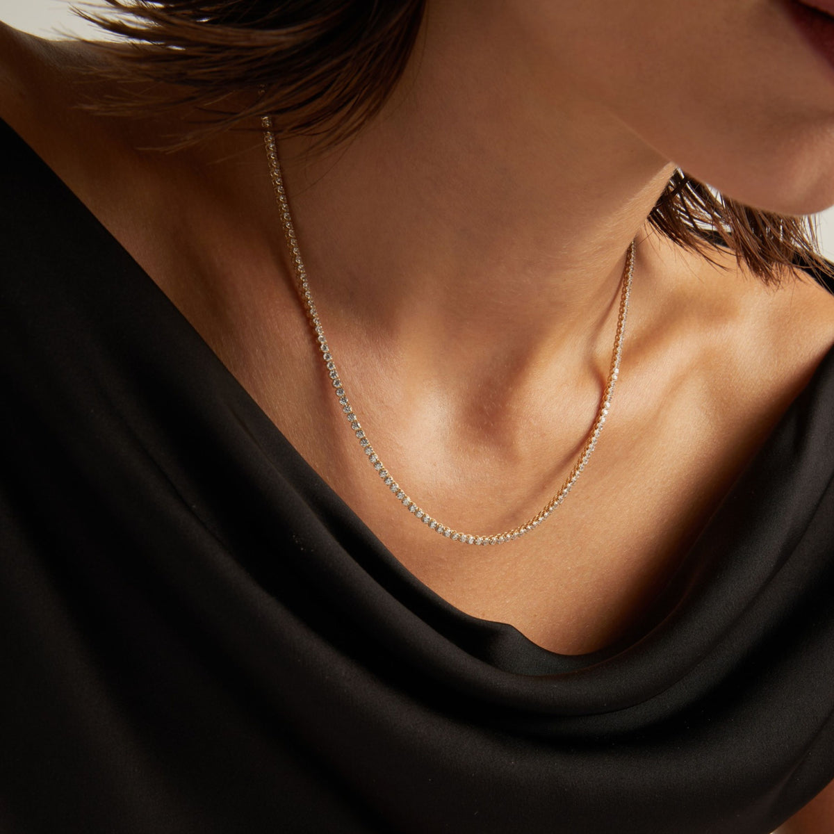 Model. Close up of a woman in a black top wearing a diamond tennis necklace on beige background.