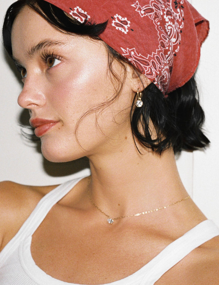 Model. Close up of woman wearing red bandana with diamond solitaire earrings and necklace on white background.