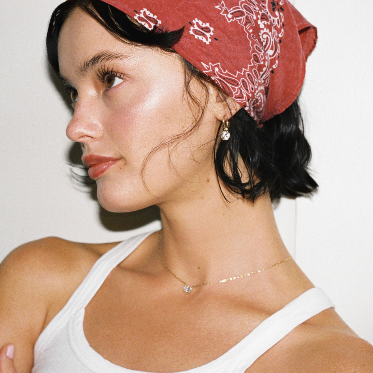Model. Close up of woman wearing red bandana with diamond solitaire earrings and necklace on white background.
