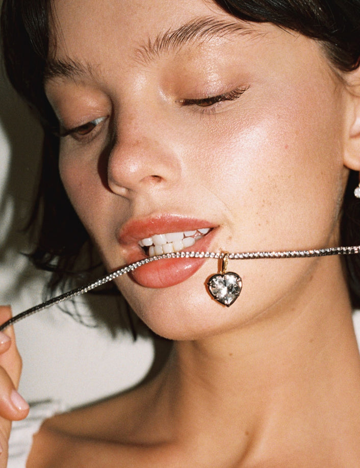 Model. Close up of woman with tennis necklace in mouth with heart gemstone pendant 