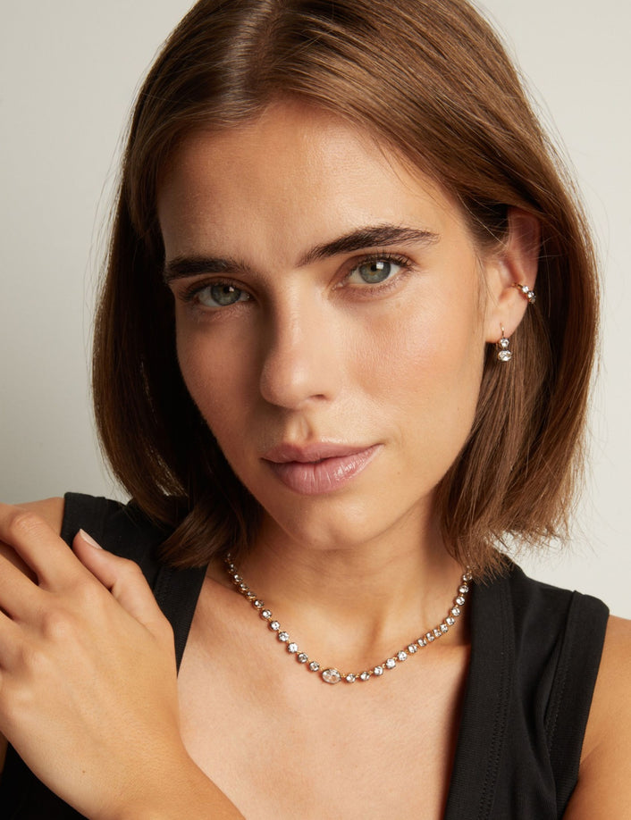 Model. Close up of woman wearing a couple gemstone earrings with a matching tennis necklace on neutral background.
