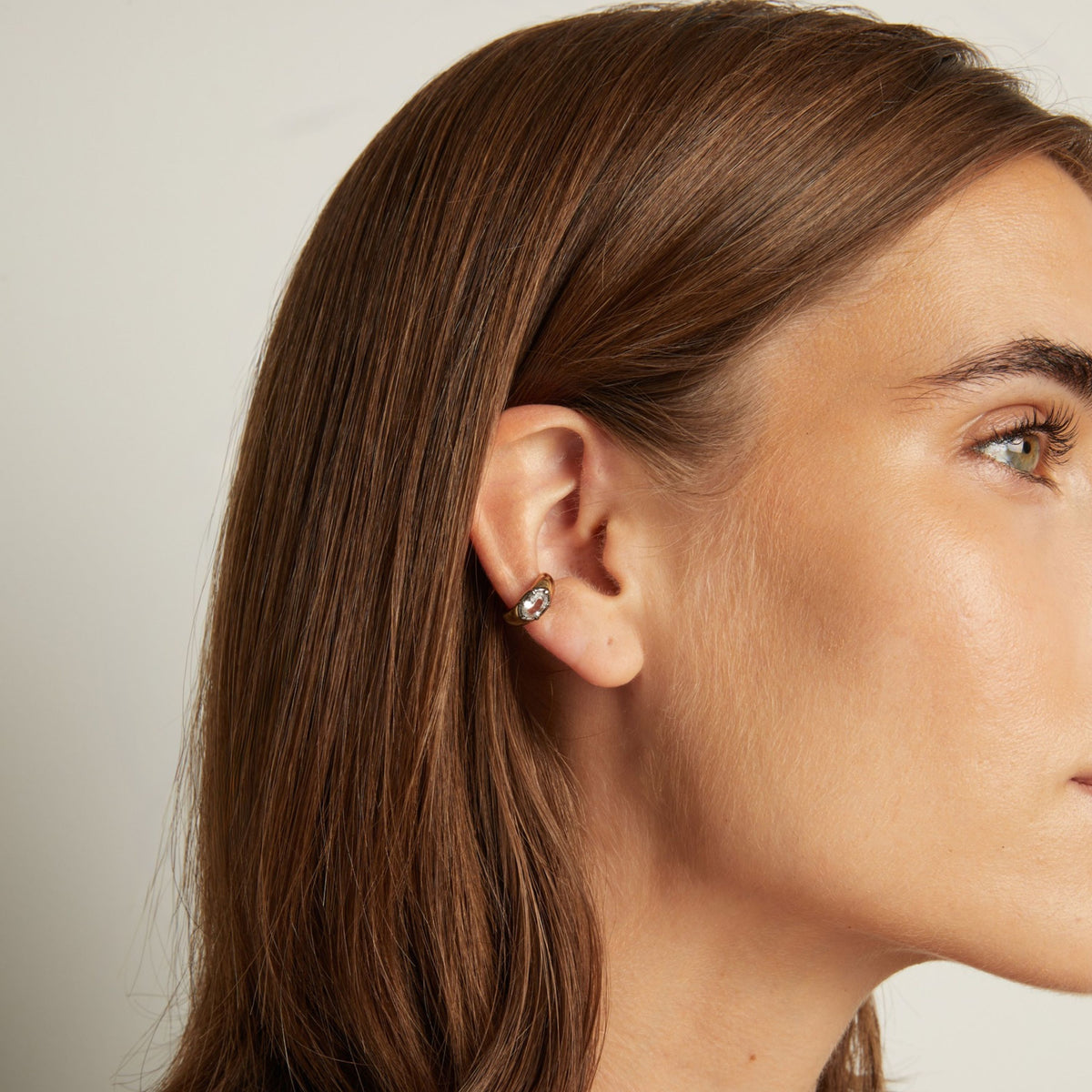 Model. Close up of woman wearing bold ear cuff on neutral background.
