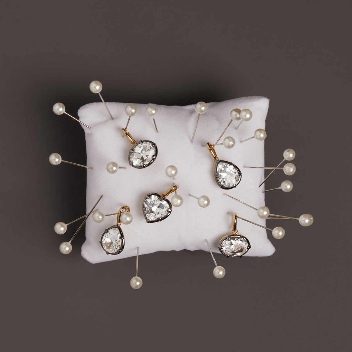 Model. Close up of black rhodium pendants on top on small white sewing pillow with sewing needles around it. 