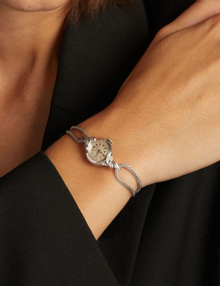 Close up of a woman wearing a silver chain watch on neutral background.