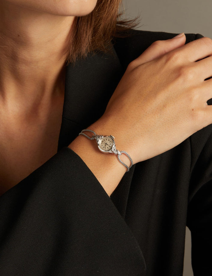 Model. Close up of a woman wearing a silver chain watch on neutral background.