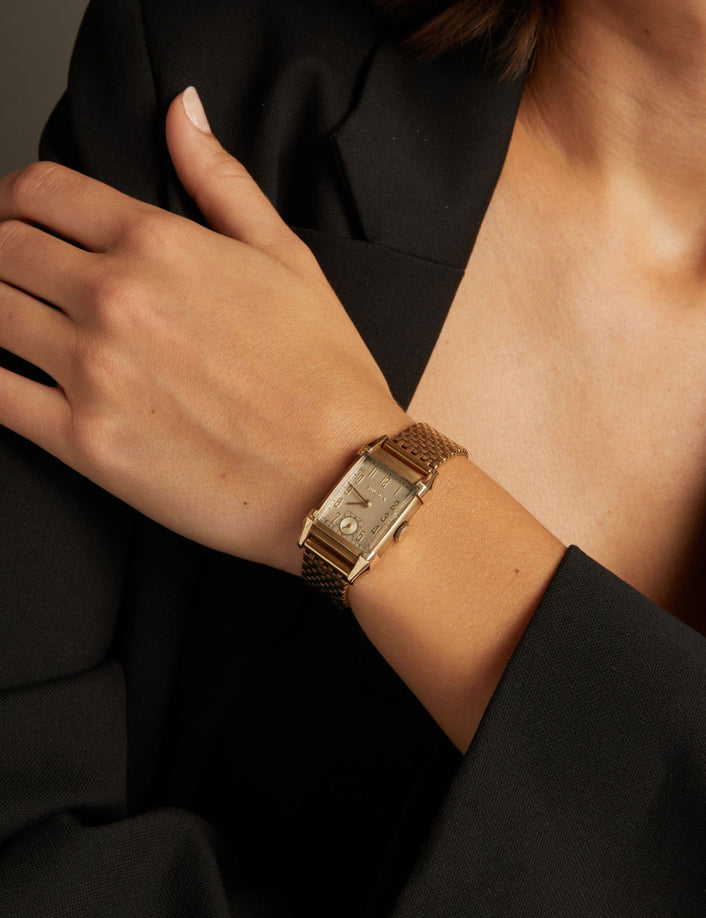 Model. Close up of a woman wearing a gold watch on neutral background.