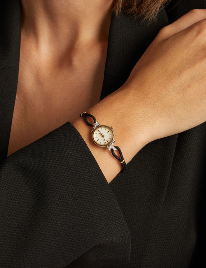 Model. Close up of a woman wearing a black rope watch with silver face on neutral background.