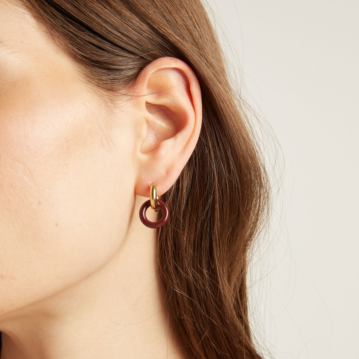 Close up of an ear wearing a gold and maroon hoop earring.