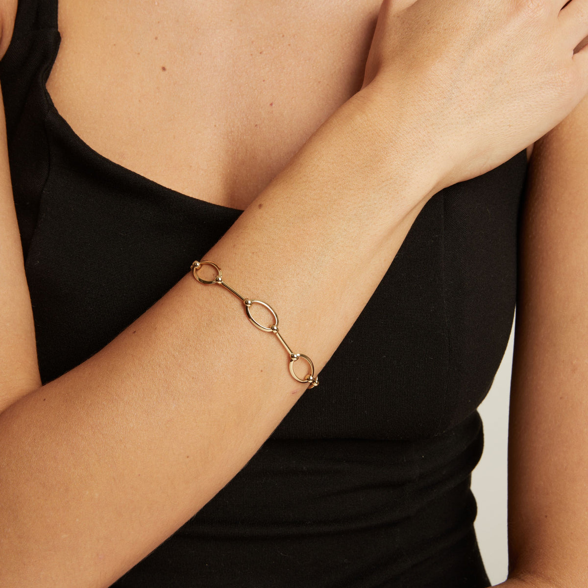 A gold chain bracelet with oval links worn on a woman's wrist, shown against a black top.